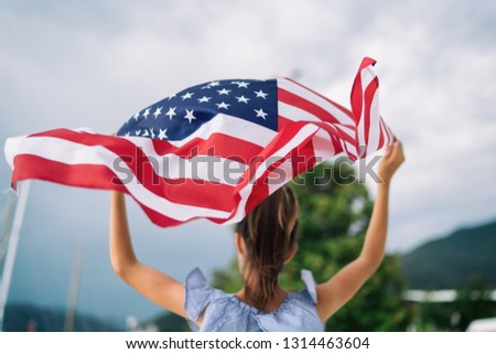 Child girl is waving American USA flag at background of the sea and yachts