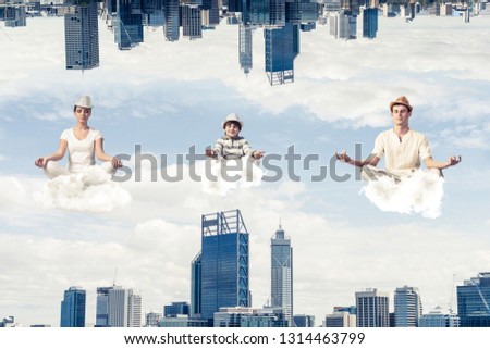 Young family keeping eyes closed and looking concentrated while meditating on clouds in the air between two urban worlds.