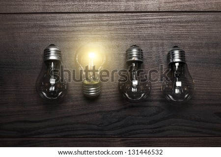 glowing bulb uniqueness concept on brown wooden background Royalty-Free Stock Photo #131446532