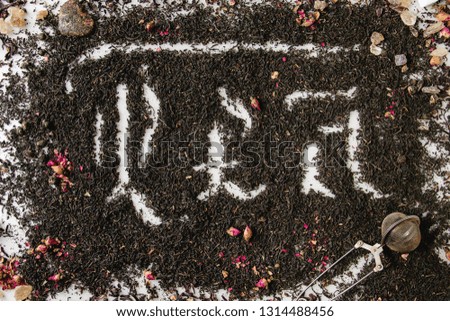Calligraphic inscription gothic letters tea over dry black ceylon and green tea scattered on white marble with rose buds and stainer. Tea drinking concept background. Top view
