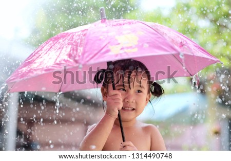Happy funny child with pink umbrella under shower. Little girl enjoying rainfall in the garden. Selective focus