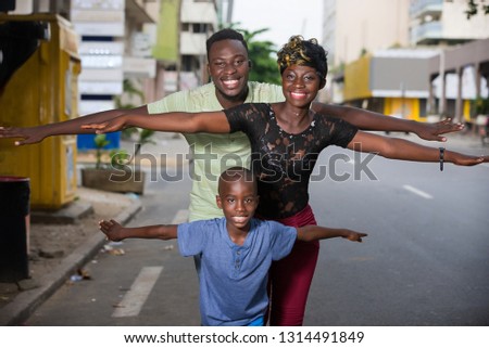Young family outdoors in a row with outstretched hands looks at the camera laughing.