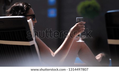 woman is drinking wine or juice lying on a lounger near a swimming pool
