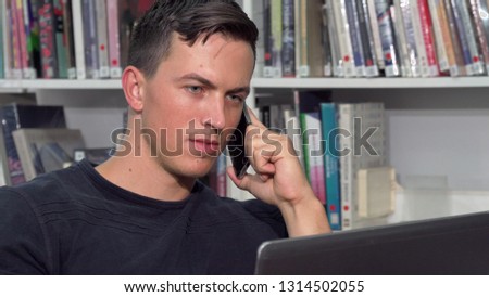 Handsome man talking on the phone, while doing homework on laptop