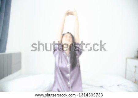 women sit at the edge of the bed. And stretching his arms to relax in the morning.Wake up in the morning. Stretching after waking.Warm tone.Do not focus on the object.Blurred image for background use.