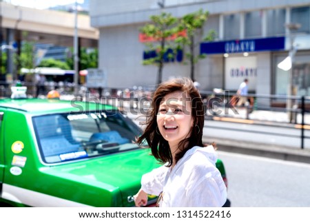Smiling Asian woman in downtown of  Hong Kong watch the camera and raising hand indicate the green taxi.