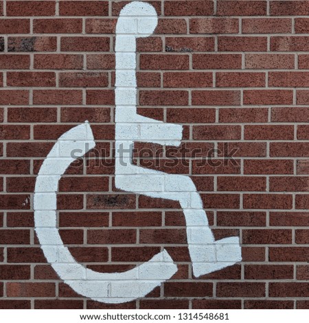 Disabled access wheelchair logo painted in white on a red brick wall