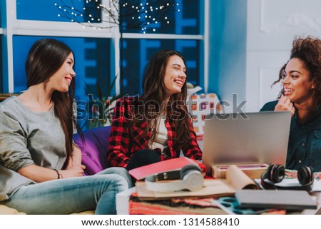 Giggly friends speaking with each other while sitting in apartment. They are in good mood. Fine concept