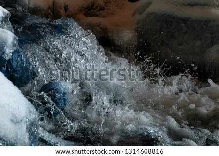 Water spray from the waves . High shutter speed picture of river water flowing, in the winter. Texture river creek stream. Waterfal