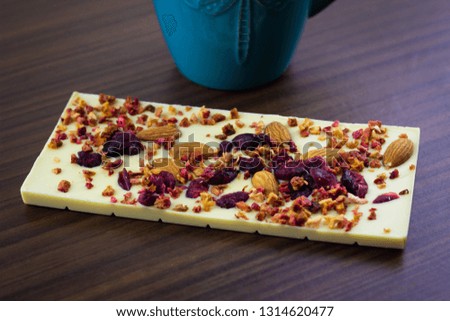 White chocolate with dried berries, candied fruits and almonds on the wooden background next to the blue mug.