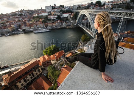 Woman with blond dreadlocks sitting in front of Douro river and Dom Luis I bridge, Porto - Portugal.