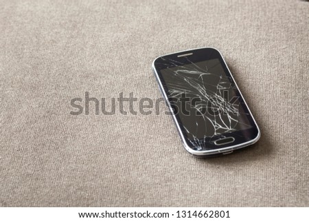 Black old cellphone with cracked screen on light cloth copy space background. Gadget repair and maintenance concept.