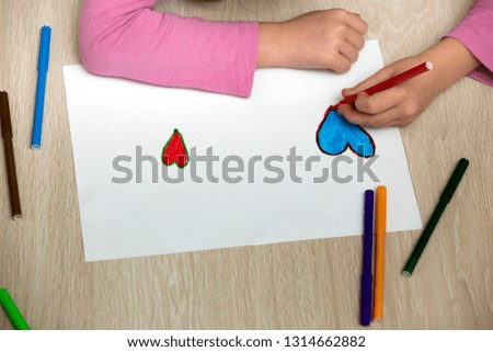 Child girl hands drawing with colorful pencils crayons heart on white paper. Art education, creativity concept.