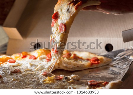  hand takes a slice of fresh pizza with  pulling  melted cheese out of the box. Food delivery