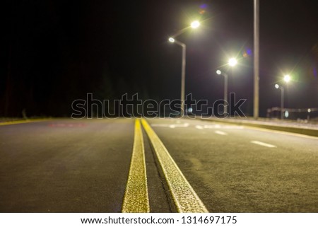 Wide modern smooth empty illuminated with street lamps asphalt highway with bright white marking sign line at night. Speed, safety, comfortable journey and professional road building concept.