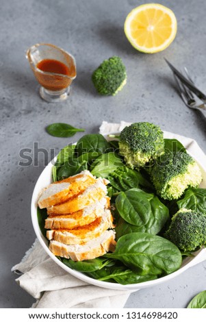 Chicken breast with spinach, broccoli and citrus dressing on a white plate. Grey concrete background. Copy space. Healthy diet lunch or dinner. Keto diet.