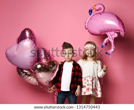 Cool little boy with color heart balloons and pretty little girl with flamingo balloon came together at the party on pink background