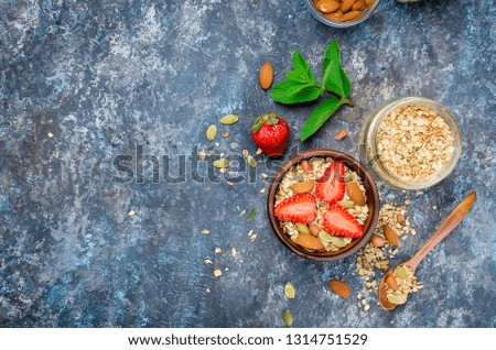 Fresh Homemade granola, muesli with strawberries, almonds, peanuts and seeds in a white plate on a dark grey background, selective focus, top view, copy space