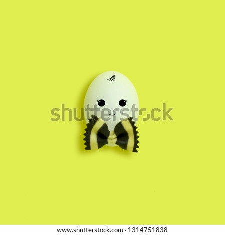 Handmade cute boy made of egg from bow of pasta farfalle. Bicolor pasta farfalle with cuttlefish ink. Creative Easter decor, kawaii style. Minimal easter concept