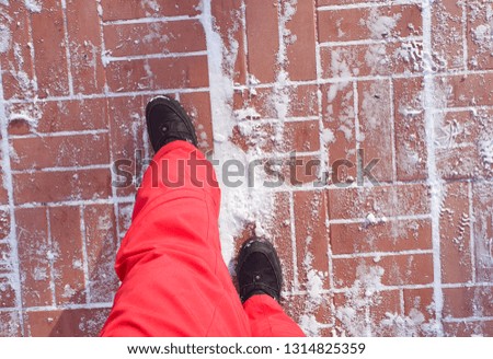 Women's feet in red warm ski pants in winter boots, standing on the pavement tiles with snow on the winter street