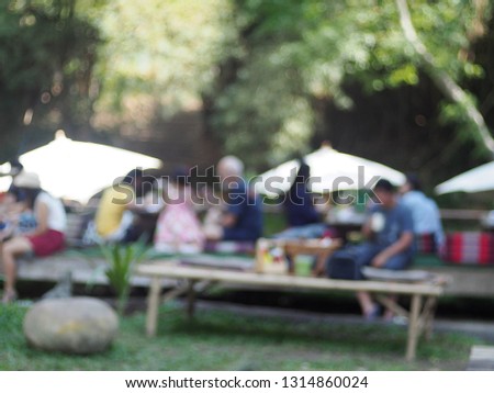 blur defocused picture of people and families with children having summer picnic on green garden near riverbank under shiny sunlight and white umbrellas for happy and relax mood summertime background