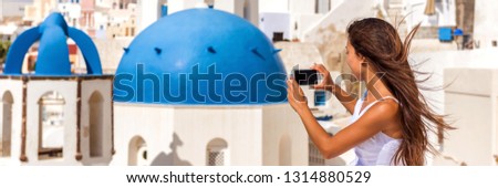 Travel tourist taking phone picture of Santorini Blue dome church, touristic attraction in Europe, Panoramic banner. European vacation banner. Woman taking smartphone photo of famous destination.
