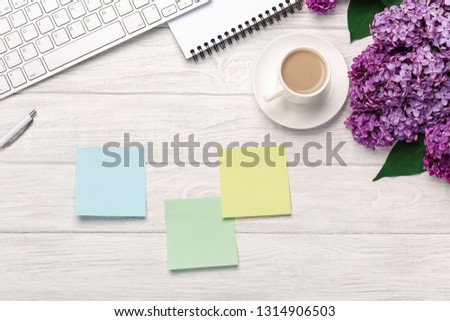 Office desktop with a bouquet of lilacs, coffee cup, keyboard, notebook and colored stickers on white boards. Top view with place for your text.