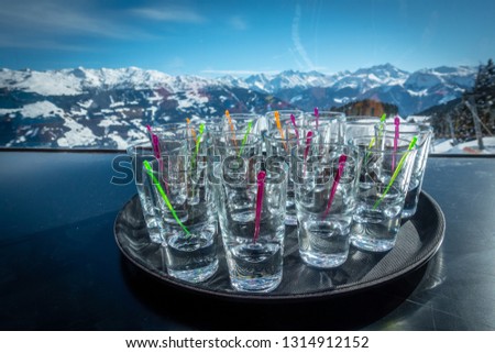 many schnapps glasses in front of a blue sky in a skiing area, drink alcohol on the slopes