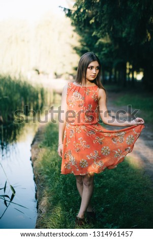 Beautiful young girl in a summer red dress in the park.
