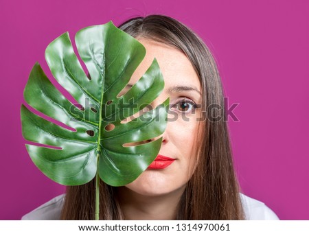 Beautiful young woman with a palm leaf on a bright background. 