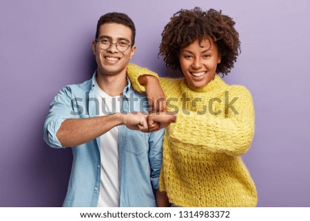 Mixed race partners give fist bump, agree to work together, have happy facial expressions rejoice success and cooperation, have toothy smiles, isolated over purple background. Team work concept Royalty-Free Stock Photo #1314983372