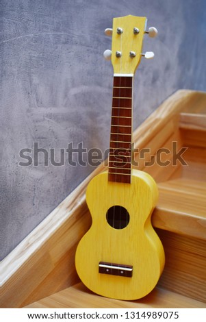 Yellow traditional soprano ukulele guitar on natural wooden stairs steps and grey grunge plaster wall background. Concept of music.
