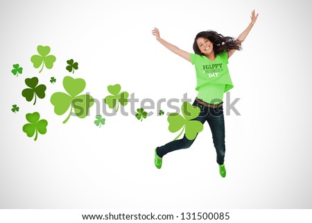 Girl wearing patricks day t-shirt jumping for joy on white shamrock background