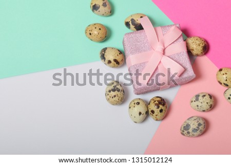 Quail eggs lie on the white surface. Next to the box with a gift wrapped in wrapping paper and tied with a ribbon. Sheets of colored paper for background.