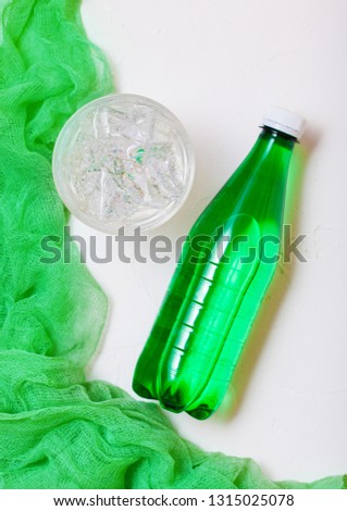 Bottle of sparkling mineral water with glass of ice and green cloth on white background
