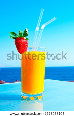 Fresh organic mango decorated with strawberries in a cafe by the sea. Fruit smoothie on the sea holiday. Vitamin drink from fresh tropical fruits. Horizontal orientation.