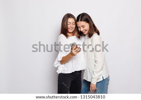 Happy smiling young woman showing photos on mobile phone to her friend. Girlfriends using electronic gadgets, chatting online, sharing news, playing games