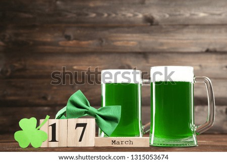 St. Patrick's Day. Green beer in mugs with cube calendar and bow tie on wooden background