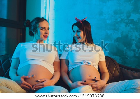 Two pregnant friends are waiting for their children showing belly.