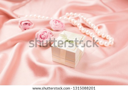 Gift festive box with silk ribbon and flowers on a gentle pink satin background. Festive concept.