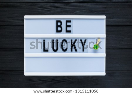 Lightbox with title Be lucky and photobooth bow tie beard on wooden sticks on black wooden background. Creative background to St. Patricks Day