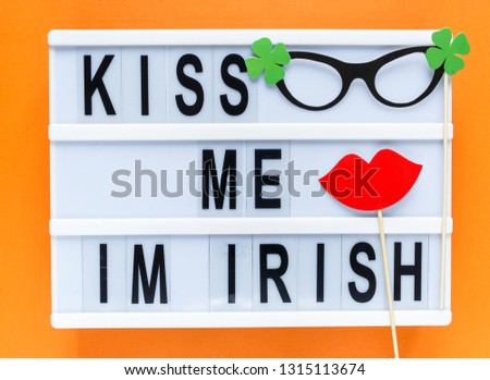 Lightbox with title Kiss me Im Irish and photobooth lips glasses on wooden sticks on black wooden background. Creative background to St. Patricks Day