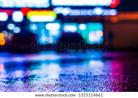 Rainy night in the city. Parking mall with cars. Reflections of shop windows on wet asphalt. Colorful colors. Close up view from the asphalt level.