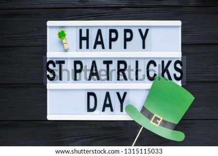 Lightbox with title Happy st Patrick Day and photobooth hat on wooden sticks on black wooden background. Creative background to St. Patricks Day