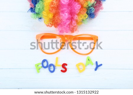 Inscription Fool's Day by colorful letters with wig and glasses on wooden table