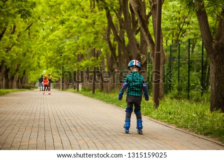 Little boy trainning on roller skates in summer green park, view from his back