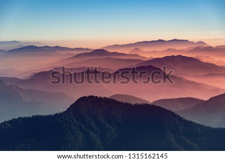 View of Himalayas mountain range with visible silhouettes through the colorful fog from Khalia top trek trail. Khalia top is at an altitude of 3500m himalayan region of Kumaon, Uttarakhand, India. Royalty-Free Stock Photo #1315162145