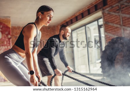 Young fitness couple in sportswear doing crossfit cardiovascular exercise using training rope at gym, healthy sports lifestyle, sport concept. Royalty-Free Stock Photo #1315162964