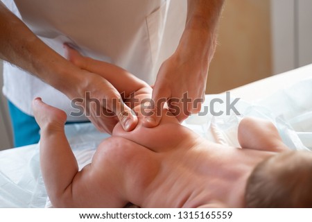 Photo from above of newborn baby and masseur hands.