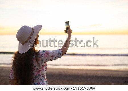 Technology, travel and holidays concept - Young woman takes pictures on the smartphone sunrise at the sea